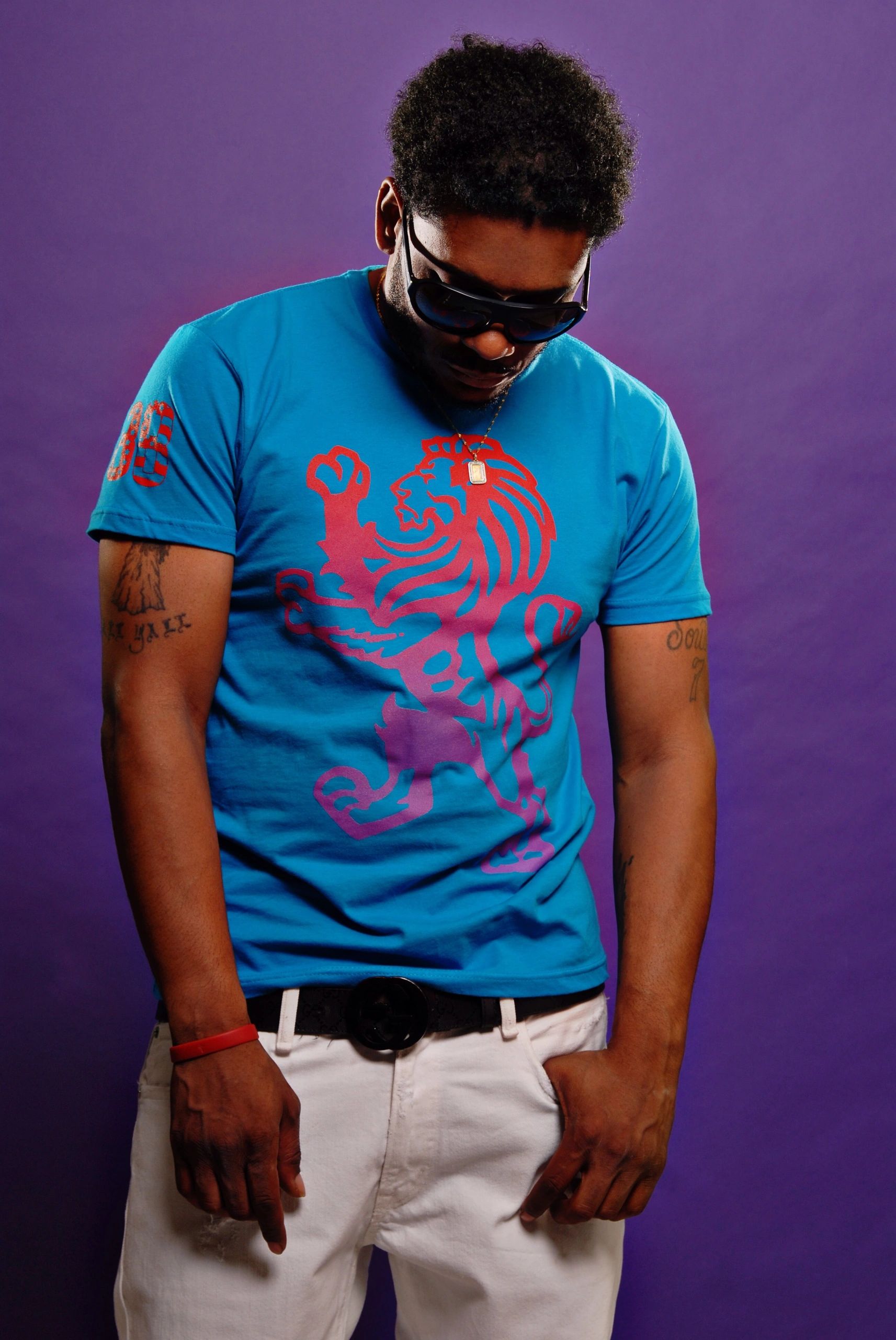 Man wearing a blue lion graphic t-shirt and white pants against a purple background.