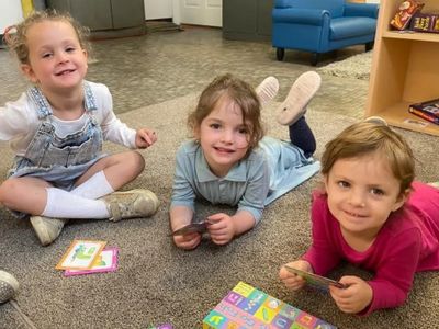 Three young children playing card games together on the floor.