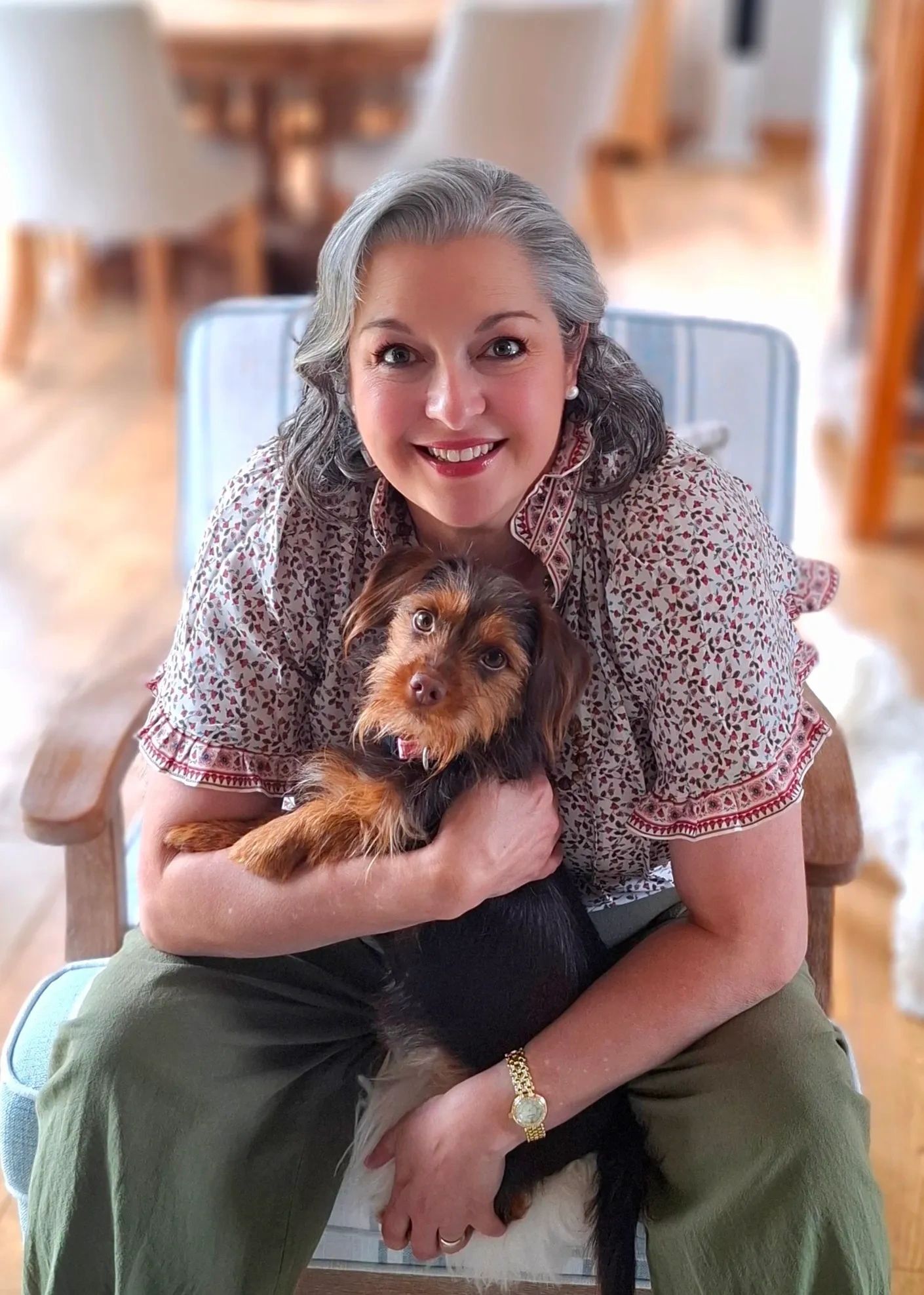 Smiling woman with gray hair holding a small brown dog.