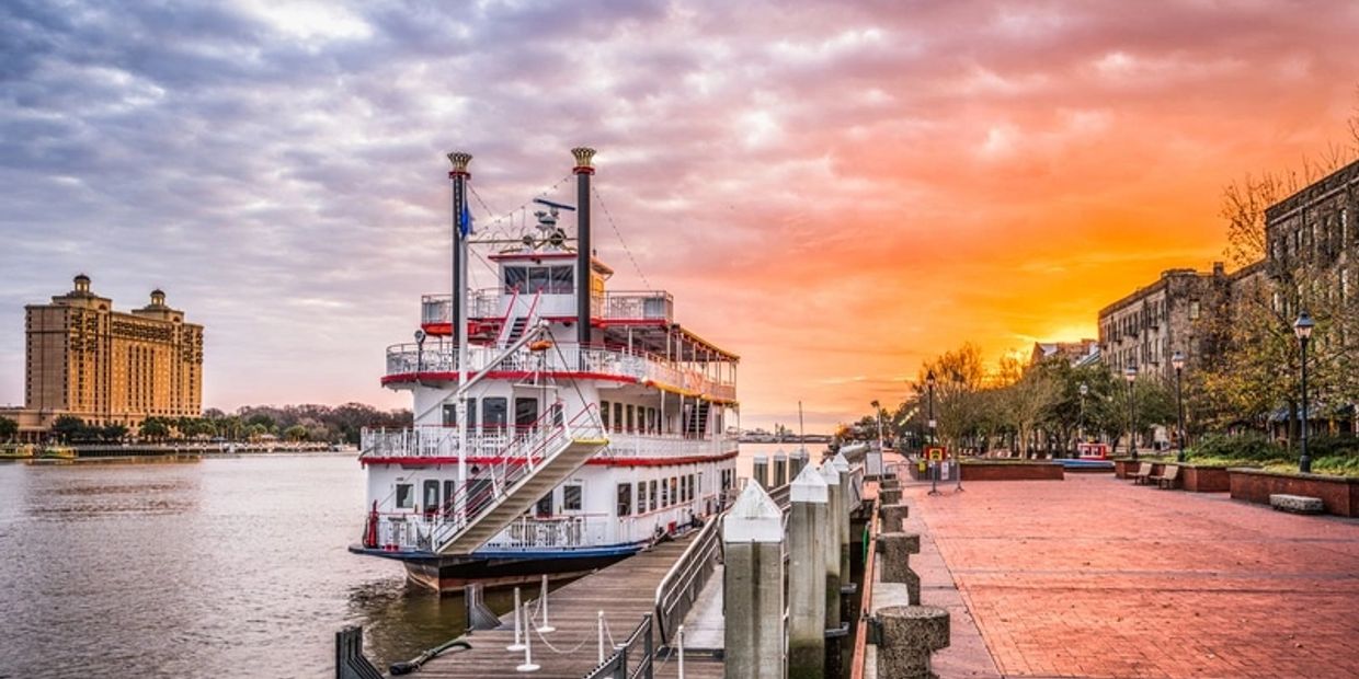 A paddlewheel riverboat docked at sunset by a city waterfront.