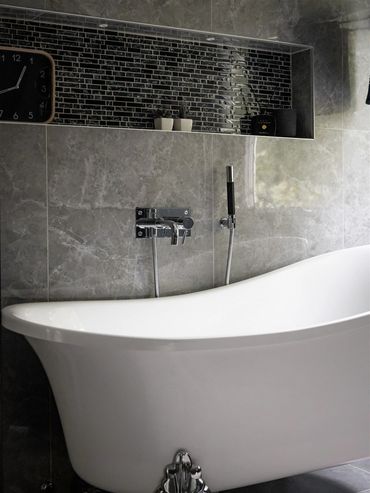 Modern bathroom with a sleek white bathtub and black tile accents.