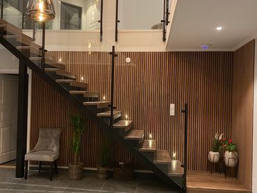 Modern staircase with wooden steps, glass railing, and warm pendant lights in a stylish living space.