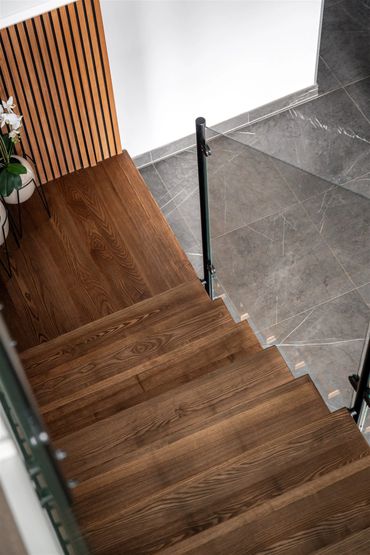 Modern wooden staircase with glass railing and marble floor below.