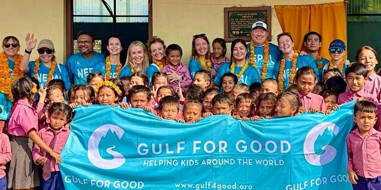 Group of volunteers and children holding a Gulf For Good banner together.