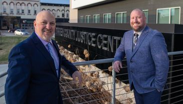 Two men in suits smile outside a justice center.