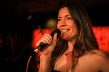 Woman singing into a microphone on stage.