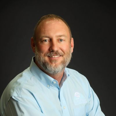 Portrait of a smiling man with a beard in a light blue shirt.