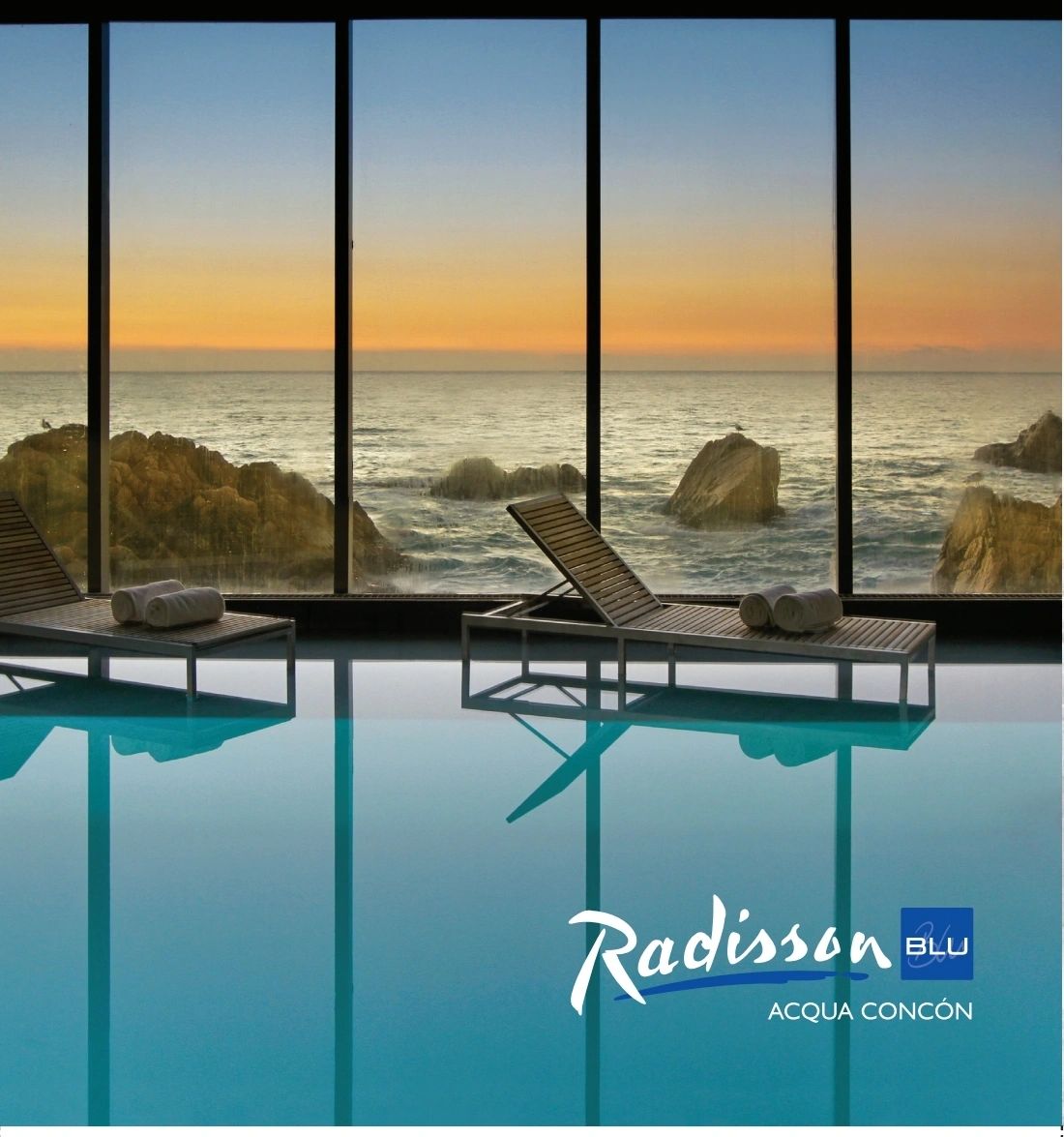 Indoor pool with ocean view at sunset and lounge chairs with towels.