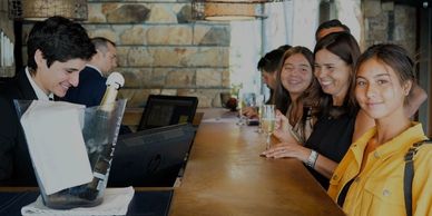 People smiling at a bar counter with a bartender serving drinks.