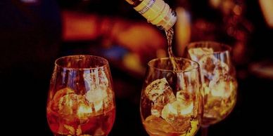 Three glasses with ice are filled with a golden liquid being poured from a bottle.