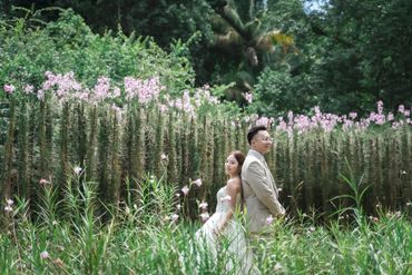 Bride and groom standing back-to-back in a lush garden filled with pink flowers.