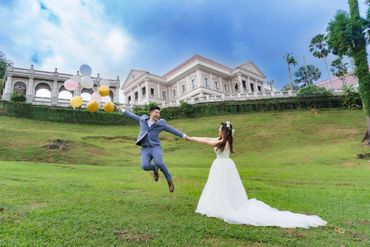 Bride and groom joyfully holding hands with balloons near a grand building.