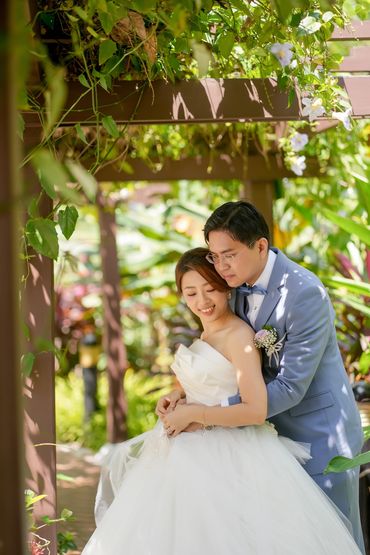 A couple embraces lovingly in a lush garden on their wedding day.