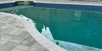 Kidney shaped in ground pool with interlock patio and concrete coping stone.