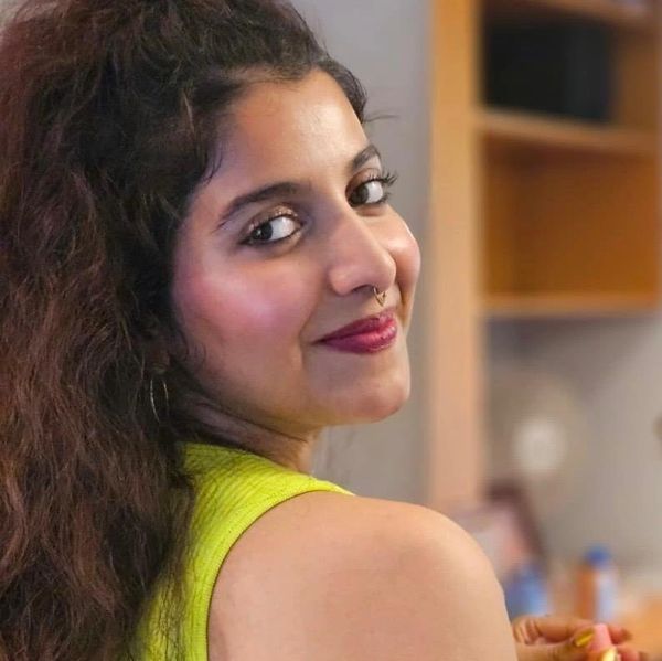 Young woman with curly hair and bright lipstick smiling over her shoulder.