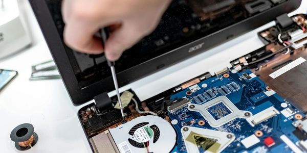 A person repairing a laptop motherboard with a screwdriver.