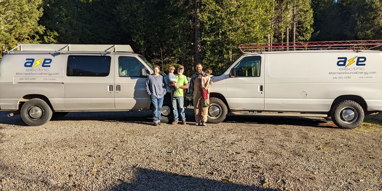 Two white vans with ASE Electric logos and four people standing between them outdoors.