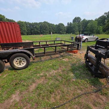 Person welding a flatbed trailer outdoors on a sunny day.