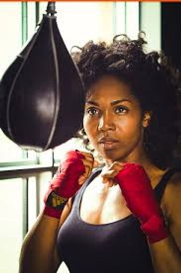 Focused woman boxer with red hand wraps training by a punching bag.