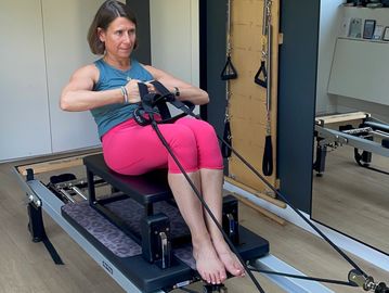 Woman exercising on a Pilates reformer machine.