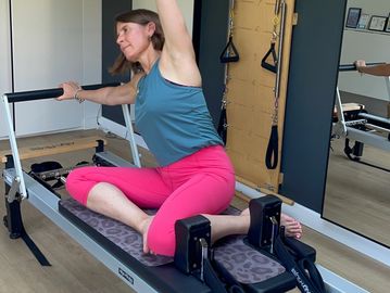 Woman stretching on Pilates reformer machine.