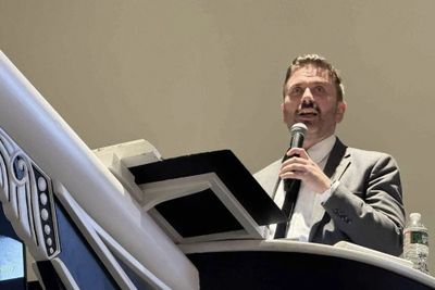 Man in suit speaking into microphone at podium.