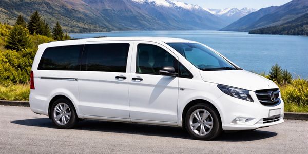White Mercedes van parked by a scenic lake with mountains.