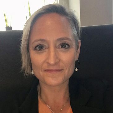 A woman with short blonde hair and pearl earrings smiling slightly.