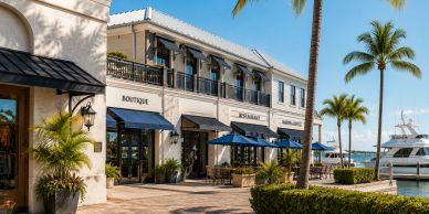Charming waterfront shops and restaurant with outdoor seating and palm trees.