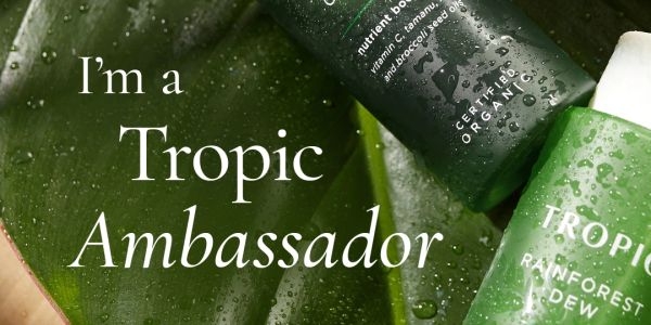 Close-up of Tropic Ambassador skincare products on wet leaves.