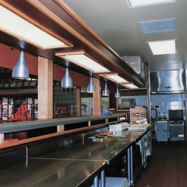 Empty commercial kitchen with stainless steel counters and industrial lighting.