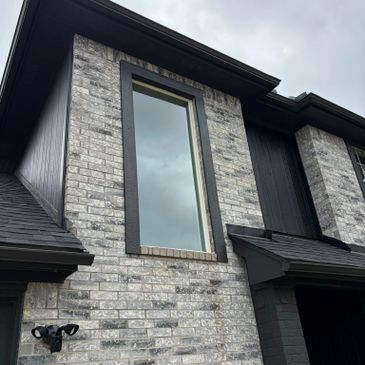 Tall window on a gray brick house under a cloudy sky.