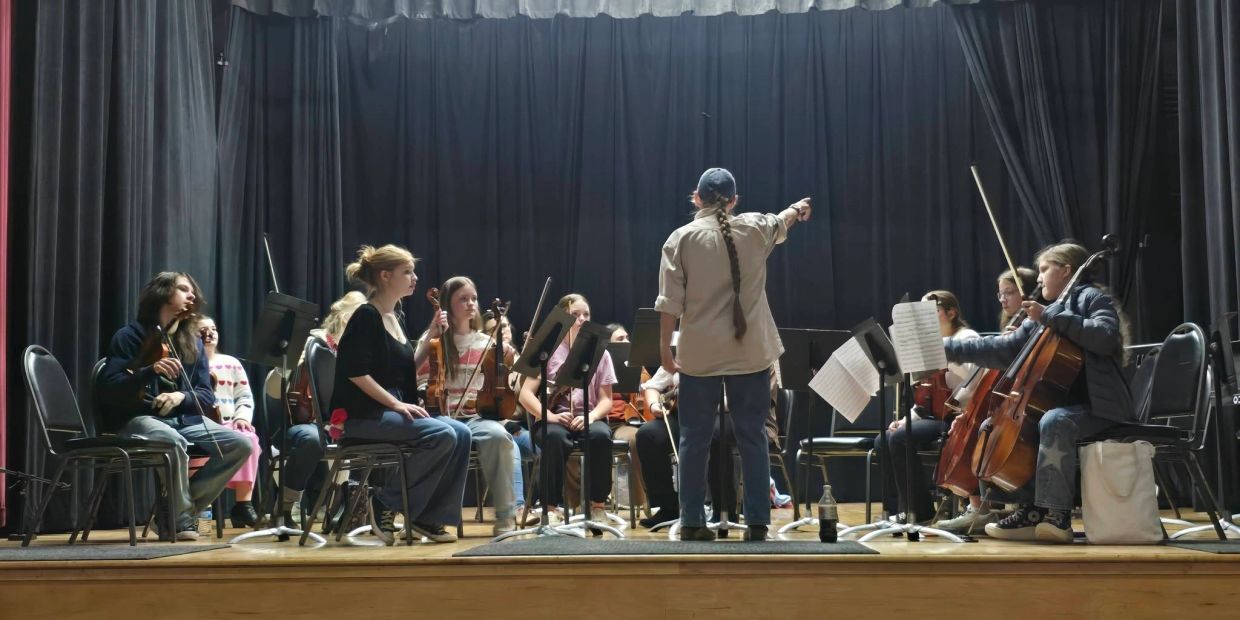 Orchestra rehearsal with conductor on stage.