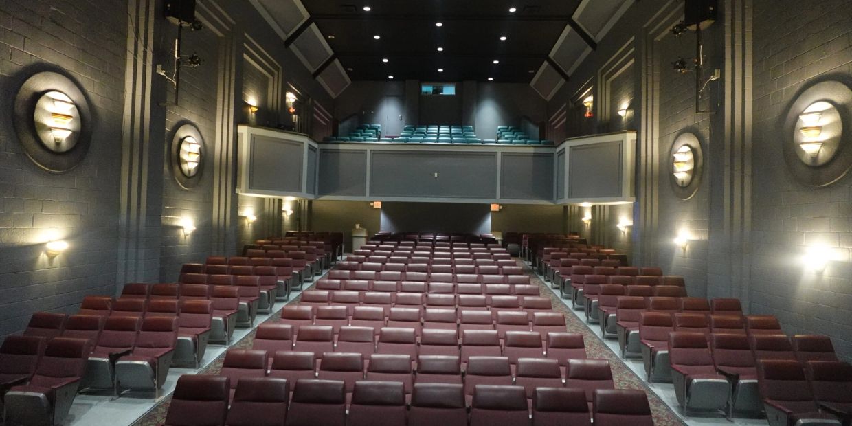 Empty vintage-style movie theater with maroon chairs and balcony seating.