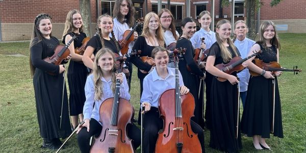 High school string orchestra group posing outdoors.