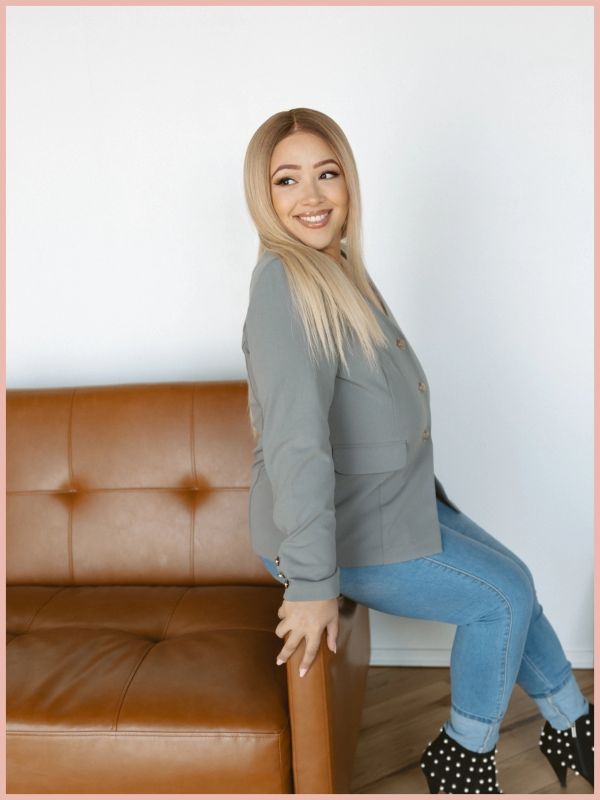 Smiling woman sitting on the arm of a brown leather sofa.