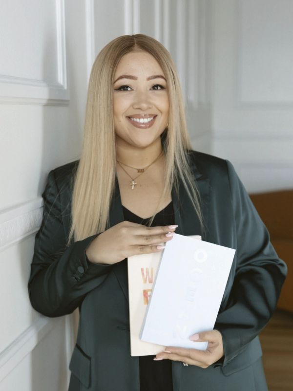 Smiling woman holding two books, wearing a black blazer.