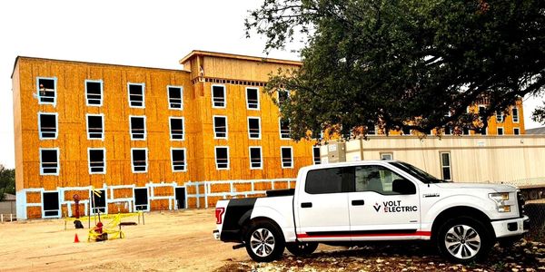 White Volt Electric truck parked near a building under construction with exposed wooden framing.