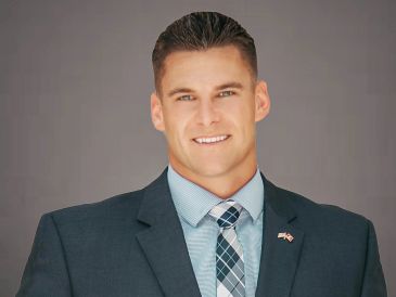 A confident man in a suit smiling against a neutral background.