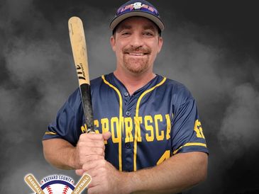 Smiling baseball player in navy and yellow jersey holding a bat.