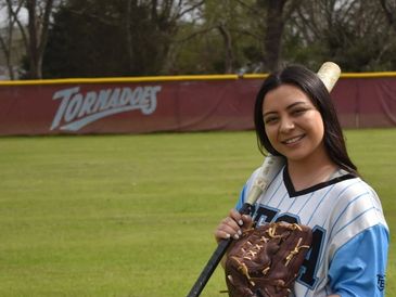 Smiling softball player posing with bat and glove on field.