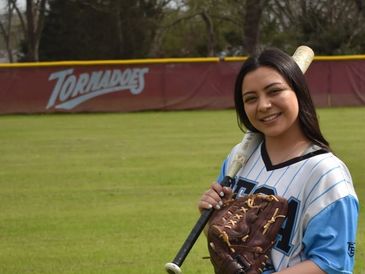 Smiling softball player posing with bat and glove on the field.