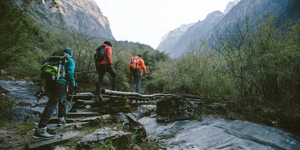 Three hikers crossing a natural bridge in the mountains.