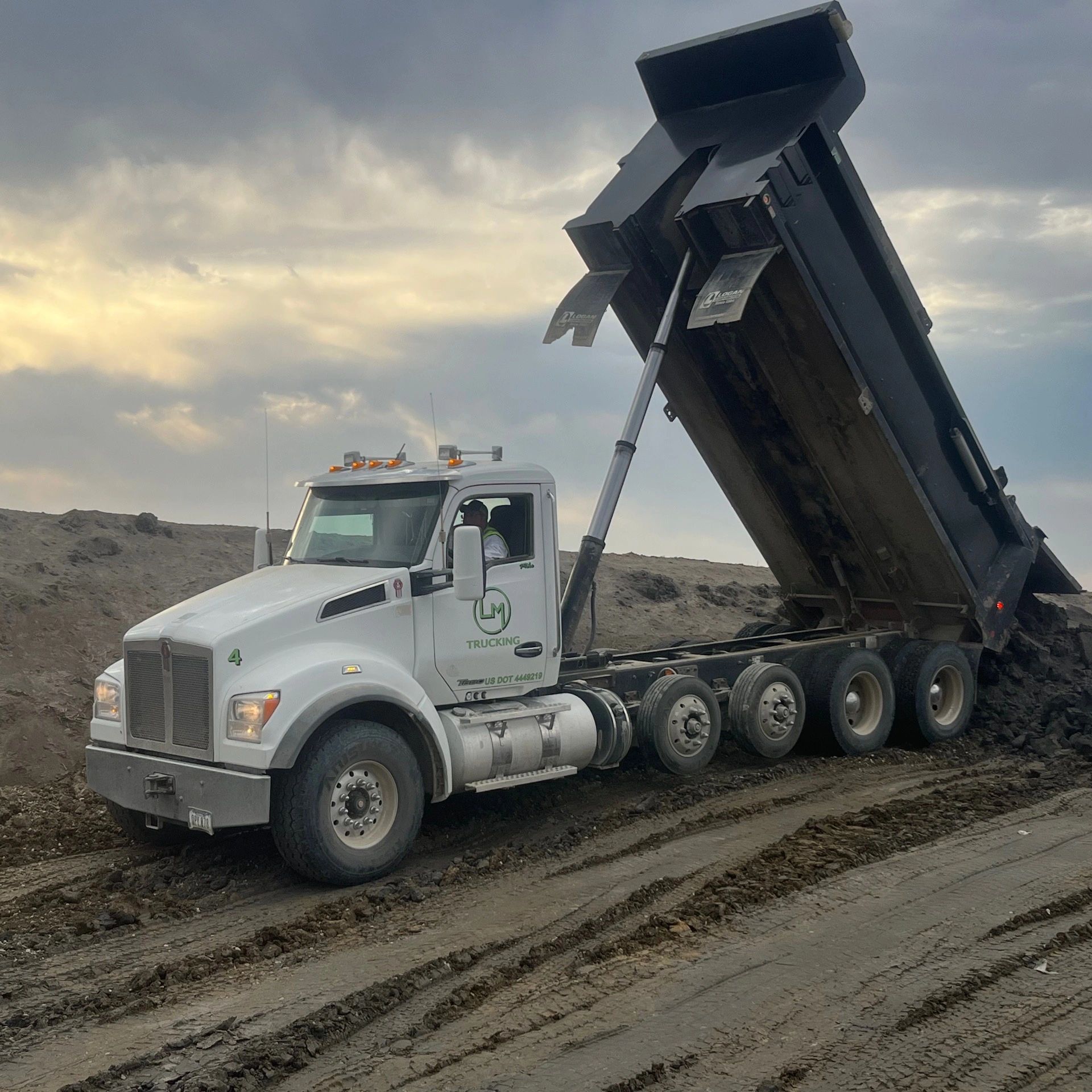 White dump truck unloading dirt on a construction site under a cloudy sky.
