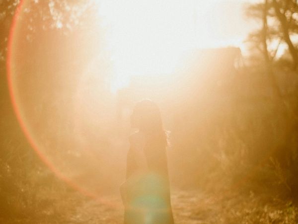 Silhouette of a person standing in warm, glowing sunlight outdoors.