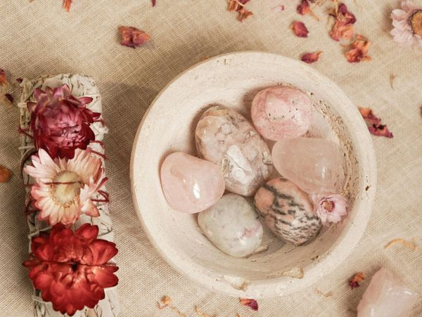 A bowl with polished rose quartz stones and dried flowers on a beige cloth.