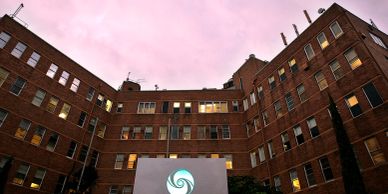 Exterior view of a brick building complex at sunset with a cloudy pink sky.