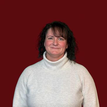Woman with dark curly hair in a white turtleneck sweater against a maroon background.