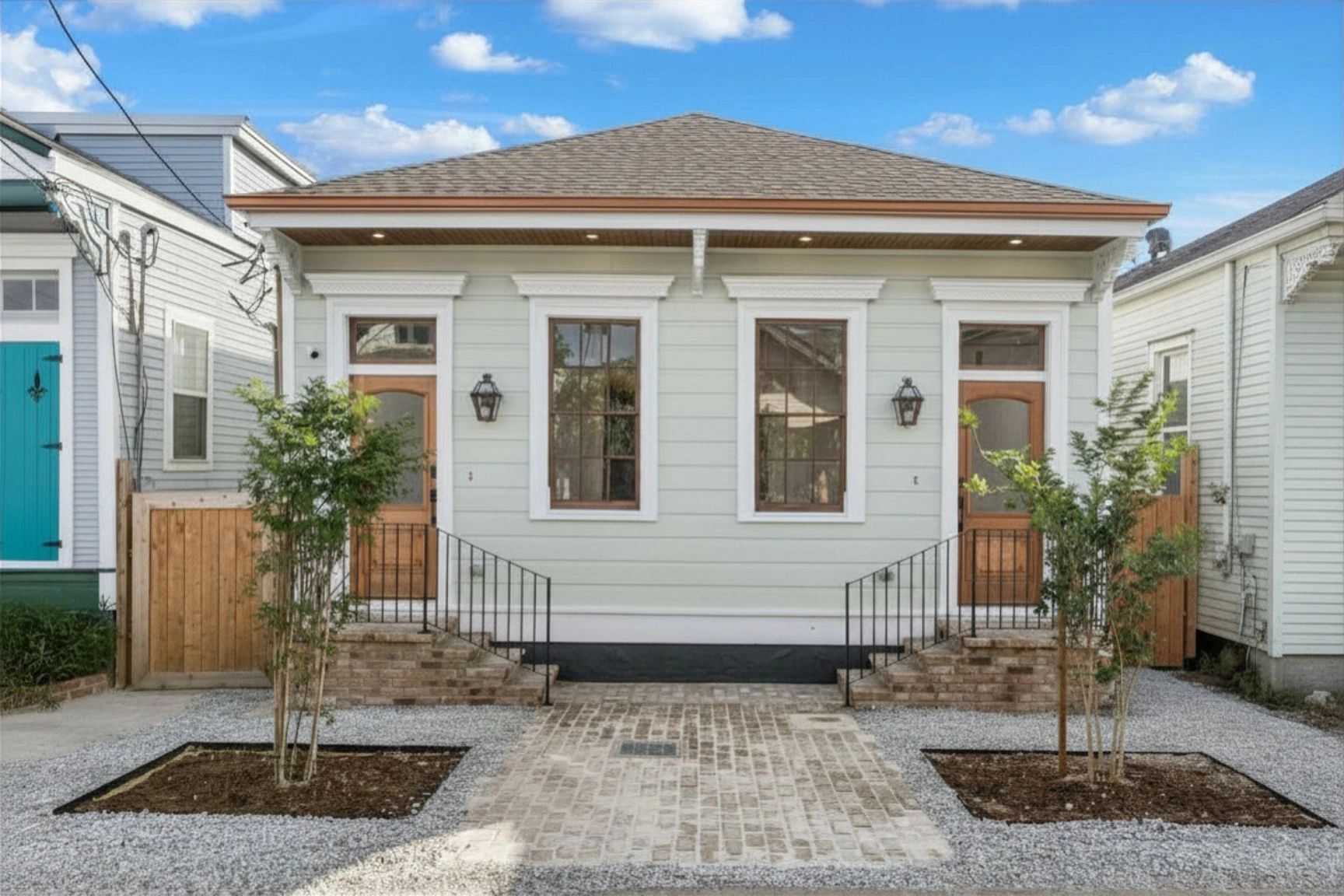 Symmetrical duplex with wooden doors and small trees in front.