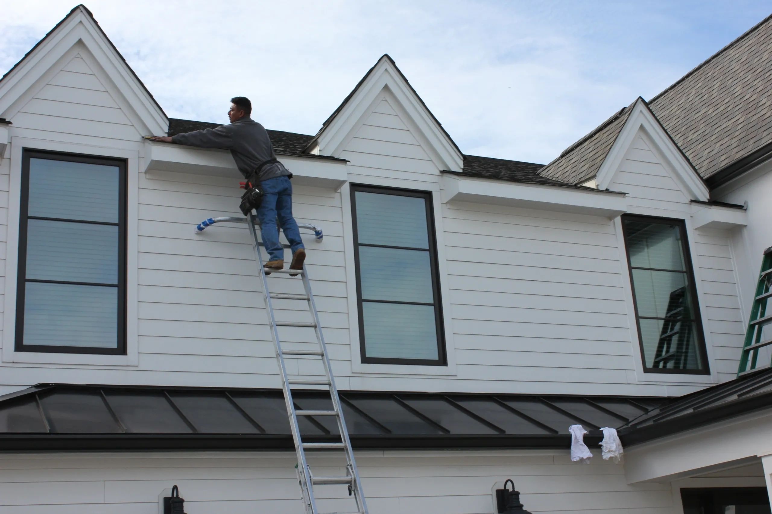 man installing roofing shingles on ladder 